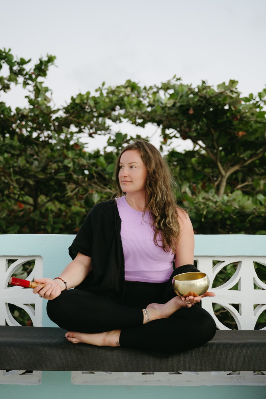 Megan seated cross-legged outdoors, holding a singing bowl