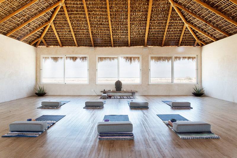 Open-air yoga studio with a thatched palapa roof and mats set out