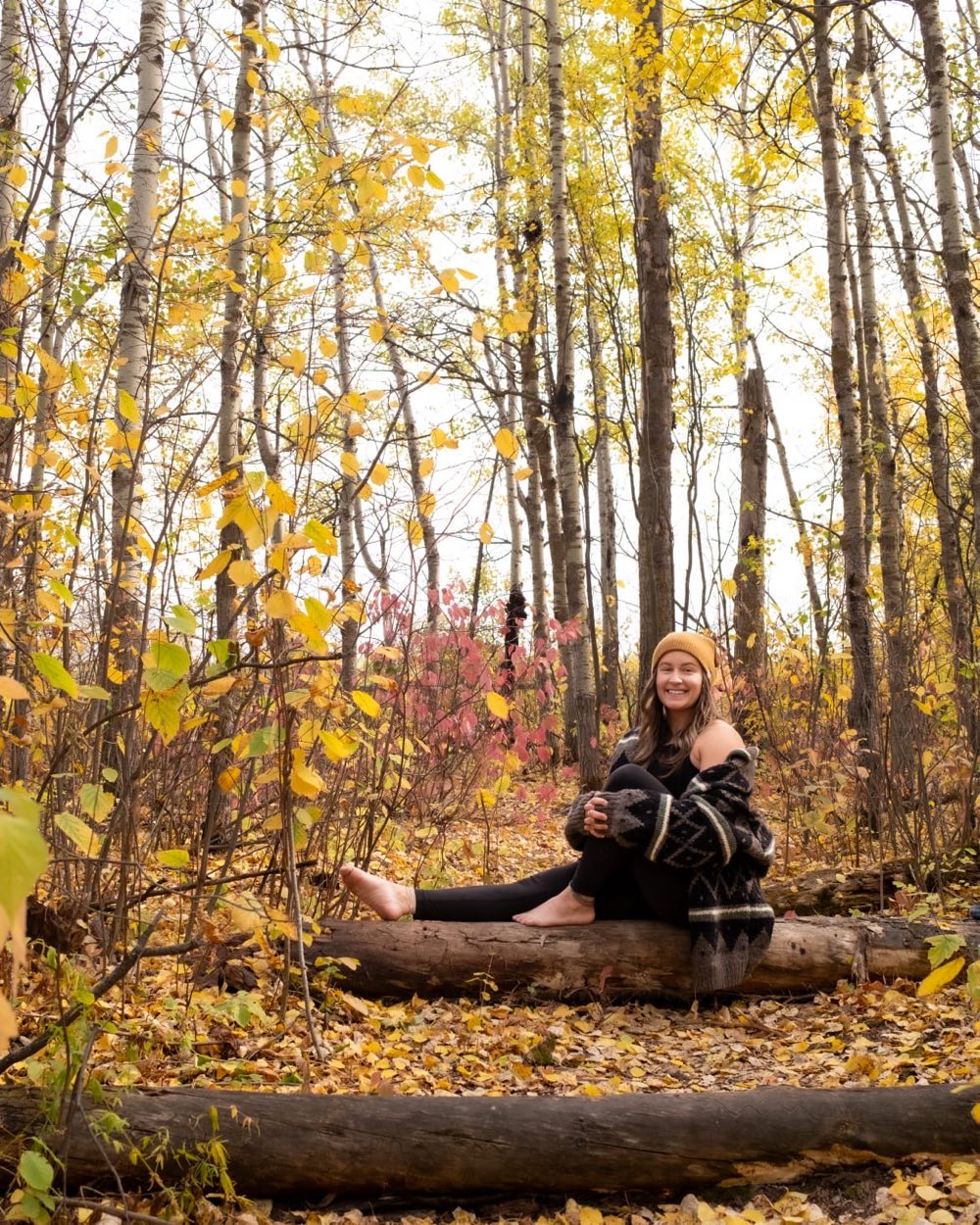 Megan smiling on a fallen log in a golden autumn forest